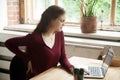 Young female office worker has back discomfort at work desk.