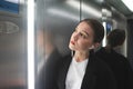 Young female office worker is standing in the lift listening to music in the headphones looking at the floor number. Businesswoman