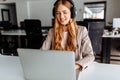 Smiling young female operator in headset works while sitting at the table, uses laptop, working in the call center Royalty Free Stock Photo