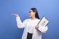 Young female ophthalmologist with glasses holding eye chart over blue background studio, healthcare concept Royalty Free Stock Photo