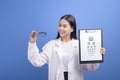 Young female ophthalmologist with glasses holding eye chart over blue background studio, healthcare concept Royalty Free Stock Photo