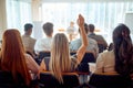 A young female participant is raising a hand to ask a question during a business lecture in the conference room. Business, people Royalty Free Stock Photo