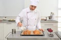 Young female pastry chef pouring chocolate sauce onto croissants at table