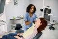 Young female patient at dental office, opening mouth while smiling African woman dentist in uniform and blue latex Royalty Free Stock Photo