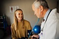 Young female patient smiling while blood pressure is tested by elderly male doctor in lab coat Royalty Free Stock Photo