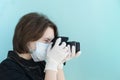 Young female photographer in medical mask and white medical gloves makes photos