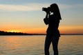 Young female photographer taking photo of riverside sunset with professional camera Royalty Free Stock Photo