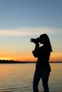 Young female photographer taking photo of riverside sunset with professional camera Royalty Free Stock Photo