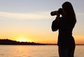 Young female photographer taking photo of riverside sunset with professional camera Royalty Free Stock Photo