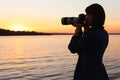 Young female photographer taking photo of riverside sunset with professional camera Royalty Free Stock Photo