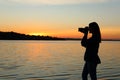 Young female photographer taking photo of riverside sunset with professional camera Royalty Free Stock Photo