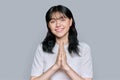 Young female pleading, holding hands in prayer on grey background