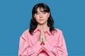 Young female pleading, holding hands in prayer request on blue background