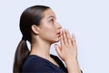 Young female pleading, holding hands in prayer on white background, profile view