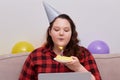 Young female plus size model blows out candles on birthday cake.