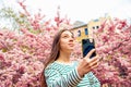 Young female posing for smartphone selfie portrait. Looking up Caucasian woman takes selfie on cherry blossom sakura flowers. Royalty Free Stock Photo
