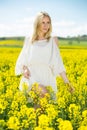 Young female posing in yellow oilseed rape field wearing in white dress Royalty Free Stock Photo