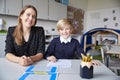 Young female primary school teacher and schoolboy sitting at a table, working one on one in a classroom, smiling to camera, front Royalty Free Stock Photo