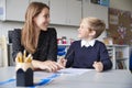 Young female primary school teacher and schoolboy sitting at a table working one on one, looking at each other smiling, front view Royalty Free Stock Photo