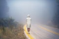 Young female in a raincoat on the road in the fog. Travel of women in the raincoat hitchhiking in the rain Royalty Free Stock Photo