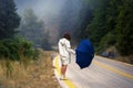 Young female in a raincoat and umbrella on the road in the fog. Travel of women in the raincoat hitchhiking in the rain Royalty Free Stock Photo