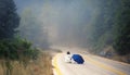 Young female in a raincoat and umbrella on the road in the fog. Travel of women in the raincoat hitchhiking in the rain Royalty Free Stock Photo