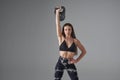 Young female with raised arm, lifting kettle bell indoors.