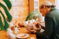 Young female reborn maker decorating newborn caucasian baby doll sitting in workshop, side view. Royalty Free Stock Photo