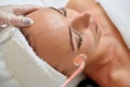 Young female receiving galvanic facial treatment in spa cosmetologist wearing gloves professional services