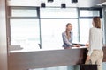 Young female receptionist looking at businesswoman signing document in office