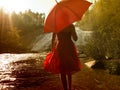 Young female with a red dress holding a red umbrella walking near a waterfall Royalty Free Stock Photo
