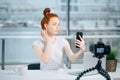 Young female redhead blogger with laptop recording video at home and take selfie