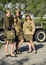 Young female reenactors dressed in uniform of Red Army soldiers of World War II standing near an old military jeep.