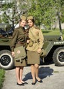 Young female reenactors dressed in uniform of Red Army soldiers of World War II standing near an old military jeep. Royalty Free Stock Photo
