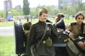 Young female reenactors dressed in uniform of Red Army soldiers of World War II standing near an old military jeep