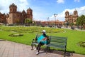 Young female relaxing on a bench at Plaza de Armas with Cusco Cathedral and the Iglesia de la Compania de Jesus in background