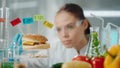 Young female researcher examines a sample of burger labeled E142, E240, E121 and E160. Biolog analyzes the quality of