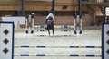 Young female rider on sorrel stallion jumping over hurdle on show jumping competition