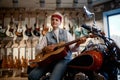 Young female rocker playing guitar at music shop sitting on motorcycle Royalty Free Stock Photo