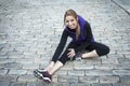 Young female runner sitting on tiled pavement in