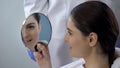 Young female satisfied with rhinoplasty result, smiling face reflected in mirror