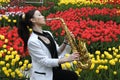 Young female saxophonist playing saxophone on a bright tulips lawn background