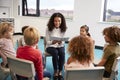 Young female school teacher reading a book to kindergarten children, sitting on chairs in a circle in the classroom listening Royalty Free Stock Photo