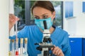 Young female scientist in uniform wearing a mask is looking through a microscope Royalty Free Stock Photo