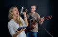 Young female singing with tablet computer in her hand. While the man playing an acoustic guitar in front of black soundproofing Royalty Free Stock Photo