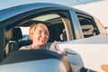 Young female sitting in car driver seat and sincerely smiling to deliveryman accepting two pizza boxes on the city street. Small