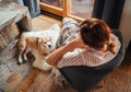 Young female sitting in comfortable chair in country house living room and dreaming and her beagle dog lying near feet on the