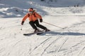 A young female skier in an orange jacket turns carving arches on the slope. A beautiful sunny day in the mountains, on the ski Royalty Free Stock Photo