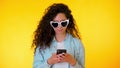 Young female smiling and using mobile phone over yellow background. Beautiful mixed race girl holding and texting with Royalty Free Stock Photo