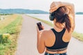 Young female starting jogging and listening to music using smartphone and wireless headphones.